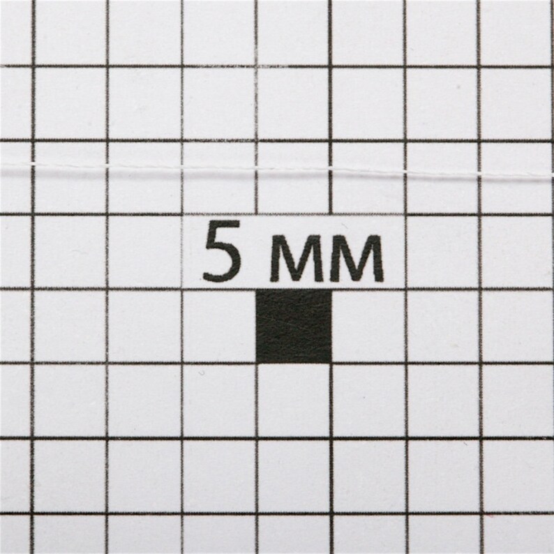 May include: A close-up of a white thread on a gridded surface with a black square and the text "5 MM".