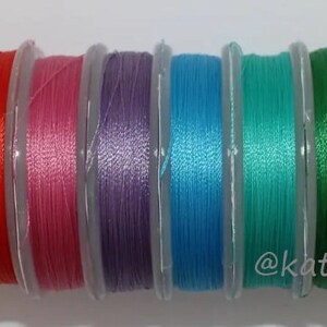 May include: A collection of ten spools of colorful thread, each wound with a different color of thread. The colors are yellow, orange, red, pink, purple, blue, teal, green, olive green, and lime green.
