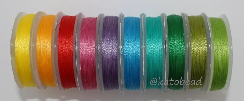 May include: A collection of ten spools of colorful thread, each wound with a different color of thread. The colors are yellow, orange, red, pink, purple, blue, teal, green, olive green, and lime green.