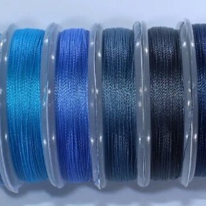 May include: Assortment of 10 spools of thread in various shades of blue and purple. The thread is wound around clear plastic spools.