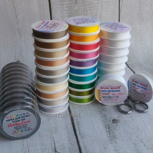 May include: Assortment of colorful spools of thread for beading, labeled "Spark Beads Tytan 100" and "Ariaina Tytan 100".