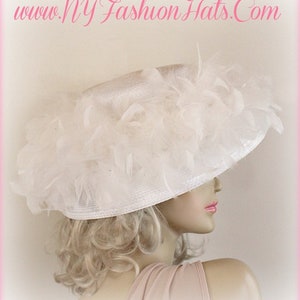 May include: A white wide-brimmed hat with a large white feather trim. The hat is made of straw and has a satin ribbon around the crown.
