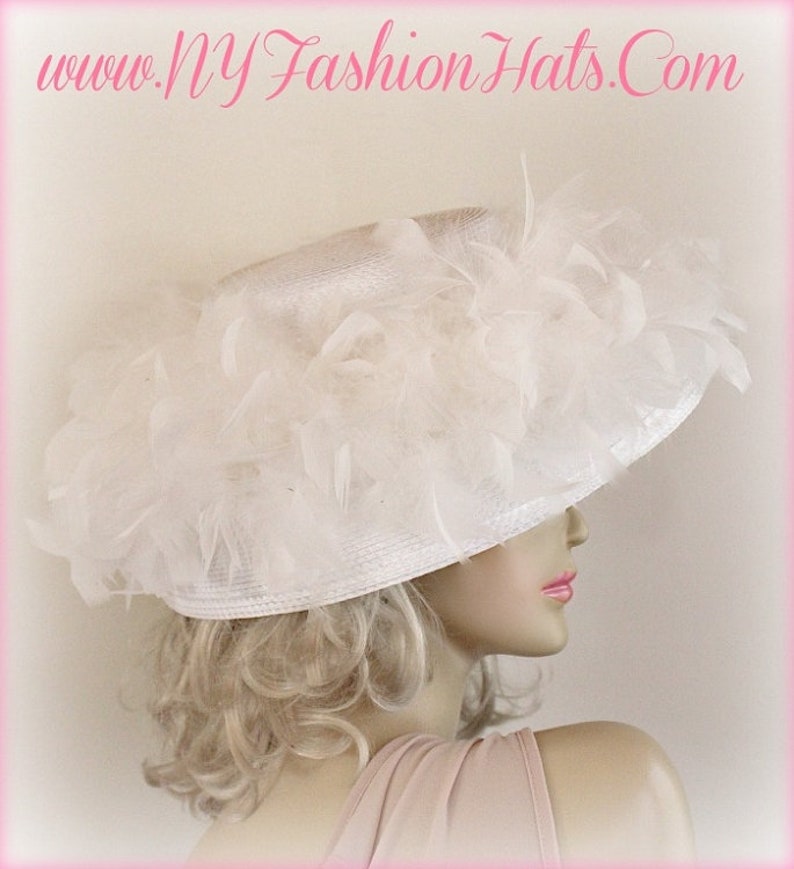 May include: A white wide-brimmed hat with a large white feather trim. The hat is made of straw and has a satin ribbon around the crown.