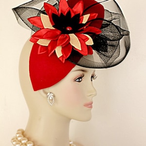 May include: A red felt hat with a black and white flower and a black net veil. The hat is worn by a mannequin with a pearl necklace. The text "NYFashionHats.com" and "Couture Designer Hats" are visible in the image.