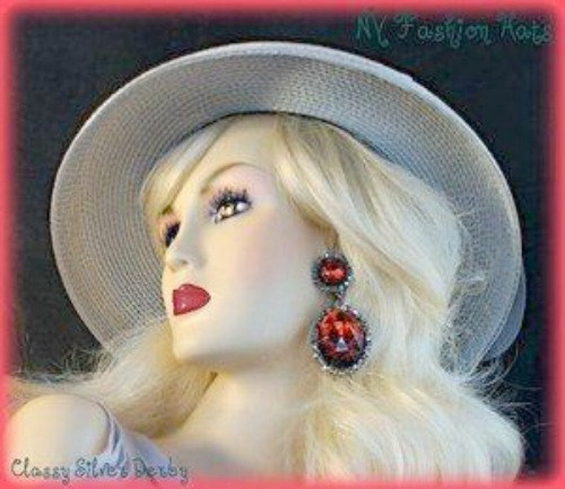 May include: A silver derby hat with a wide brim and a simple design. The hat is being worn by a mannequin with blonde hair and red earrings. The text "Classy Silver's Derby" is visible at the bottom of the image.
