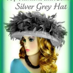 May include: A silver grey hat with a large black feather trim. The hat is made of a soft, silky material and has a wide brim.