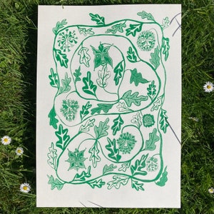 May include: A green and white print featuring stylized faces and oak leaves. The artwork is arranged in a circular pattern, with the faces interspersed among the leaves. The print is on a white background.