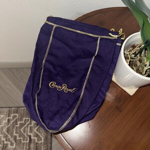 May include: A deep purple drawstring bag with gold stitching and the words "Crown Royal" in gold script. The bag is made of a soft, velvety material and is likely used for storing a bottle of liquor.