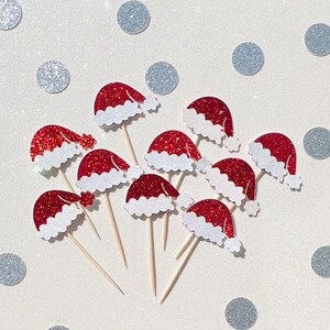 May include: Ten red and white glitter Santa hats on wooden sticks. The hats are perfect for decorating cupcakes or other treats.