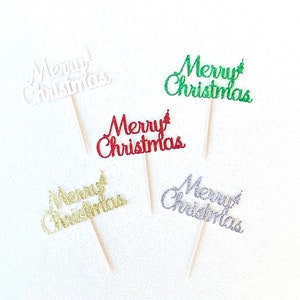 May include: Five cupcake toppers with the words "Merry Christmas" in different colors. The toppers are made of glitter and are attached to wooden sticks.