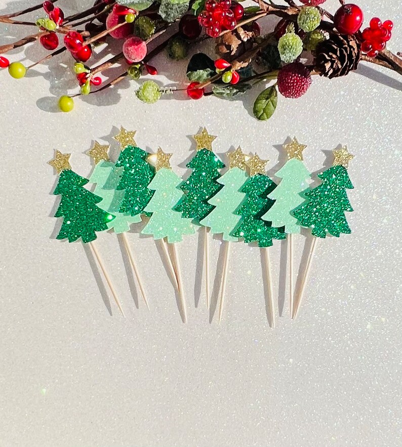 May include: A set of ten green glitter Christmas tree cupcake toppers with gold star accents. The toppers are on white sticks and are perfect for decorating cupcakes or other desserts.