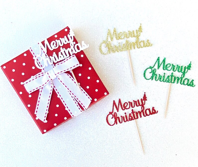 May include: Four "Merry Christmas" cake toppers with a red polka dot gift box. The toppers are made of glitter paper and come in white, gold, green, and red.