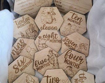 Könnte beinhalten: Holz-Meilensteinkarten für Babys mit eingravierten Winnie-the-Pooh-Figuren und Monaten. Das Set enthält Karten für "Hello World" und die Monate eins bis zwölf. Jeder Marker hat eine einzigartige sechseckige Form.