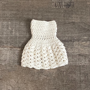 Può includere: Un abito da bambola bianco all'uncinetto con un design semplice.