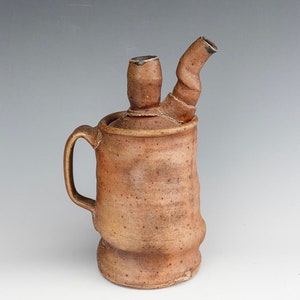 Puede incluir: Una jarra de cerámica marrón con un pico único y una asa. La jarra tiene un esmalte moteado y un cuerpo redondeado.