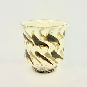 May include: A white ceramic cup with a brown and white swirl pattern. The cup has a rounded bottom and a wide opening.