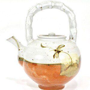May include: A white ceramic teapot with a brown and white glaze. The teapot has a bamboo-shaped handle and a lid with a knob. The teapot is decorated with a brown and white floral design.