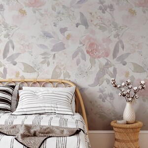 May include: A bedroom scene featuring a floral wallpaper with pink and purple watercolor flowers. A bed with striped bedding and pillows is in the foreground, along with a woven headboard and a small side table with a vase of cotton stems.