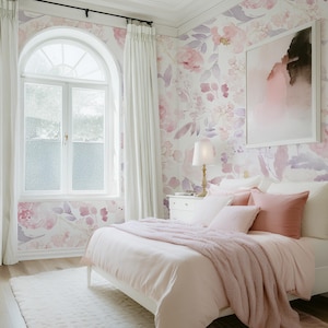 May include: A bedroom with a white bed, pink bedding, and a fluffy pink throw. The walls are decorated with floral wallpaper in shades of pink and purple. A large window with white curtains and a white rug complete the room.