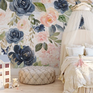 May include: A bedroom scene featuring a floral wallpaper with navy and blush roses. A bed with a canopy, a dollhouse, and a patterned ottoman are in the foreground. A teddy bear sits on the bed. The room has a soft, feminine aesthetic.
