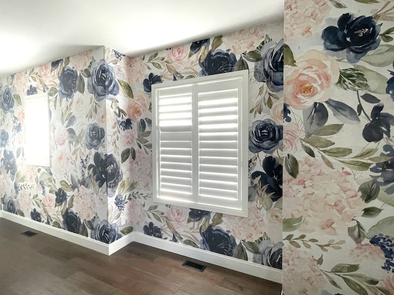 May include: Floral wallpaper featuring large navy blue and blush pink roses and hydrangeas on a white background. The wallpaper covers the walls of a room with white window shutters and a dark wood floor.