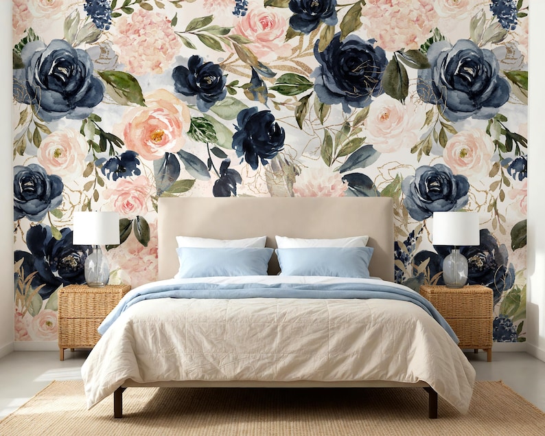 May include: A bedroom scene featuring a beige upholstered bed with light blue bedding, flanked by two wicker nightstands with white lamps. The wall behind the bed is covered in wallpaper with a watercolor floral pattern of navy and blush roses.