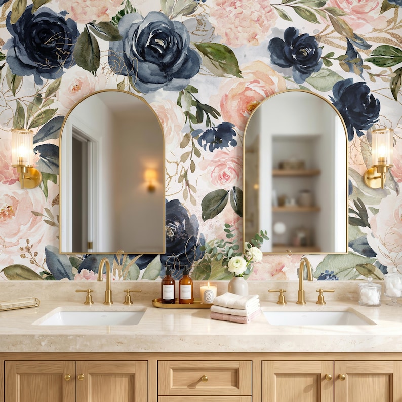 May include: A bathroom vanity featuring two arched mirrors mounted on a wall with floral wallpaper in shades of navy blue, blush pink, and green. The vanity has two white sinks, gold faucets, and light wood cabinets with gold hardware.