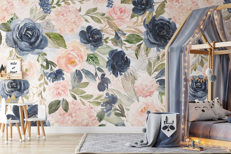 May include: A wall mural featuring a watercolor floral pattern with large navy blue and soft pink roses, green leaves, and gold accents. The design includes a small sign with the text Wild at Heart and a child's bed frame with draped fabric.
