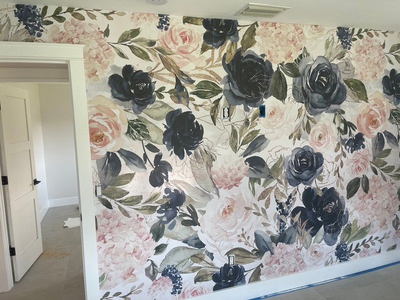 May include: Wallpaper featuring a large-scale floral pattern with watercolor-style roses and hydrangeas in shades of navy blue, blush pink, and sage green on a white background, accented with gold-toned leaf outlines and botanical foliage.