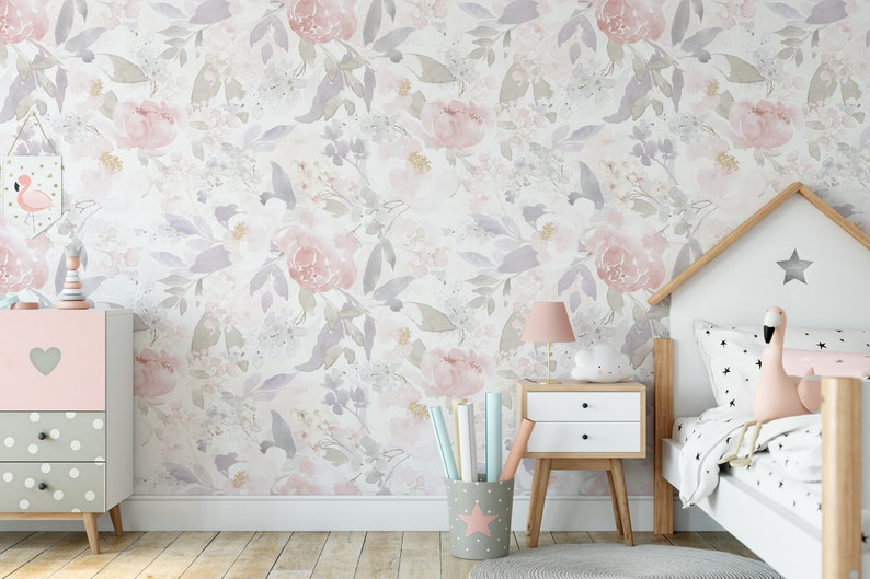 May include: A floral wallpaper featuring watercolor-style pink and purple flowers and leaves. A pink and gray dresser with a heart detail and a white nightstand with a pink lamp are in the room. A bed with a house-shaped headboard is also visible.