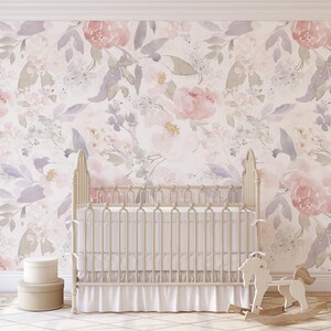 May include: A nursery scene featuring a white crib with a ruffled skirt, set against a floral wallpaper in soft pinks, purples, and greens. A wooden rocking horse and two round boxes complete the decor.