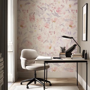 May include: A home office with a floral wallpaper in shades of pink and purple. A beige desk with a black lamp, books, and office supplies sits in front of the wallpaper. A beige chair with black legs is in front of the desk.