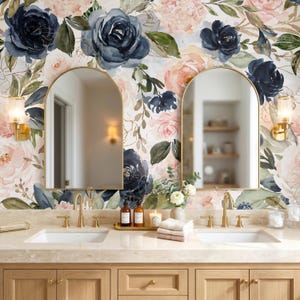 May include: A bathroom vanity featuring two arched mirrors mounted on a wall with floral wallpaper in shades of navy blue, blush pink, and green. The vanity has two white sinks, gold faucets, and light wood cabinets with gold hardware.