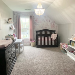 May include: A nursery room with a dark brown crib, a changing table, and a white bookshelf. The walls are painted light gray with floral wallpaper. A chandelier hangs from the ceiling, and the room is carpeted.