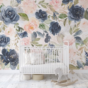 May include: A white crib with a floral wallpaper backdrop featuring navy, blush, and peach roses with gold accents. A pillow with "Good night" text rests inside the crib. A wooden rocking horse and two baskets are on the floor.