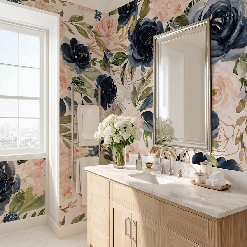 May include: A bathroom vanity with a light wood cabinet and white marble countertop, featuring a rectangular mirror, a silver towel rack with white towels, and a vase of white flowers against a floral wallpaper with navy and blush pink roses.