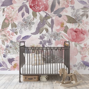 May include: A nursery scene featuring a wrought iron crib with a white mattress and a plaid pillow. The backdrop is a floral watercolor wallpaper in shades of pink, purple, and gray. A wooden rocking horse and a small suitcase are also present.
