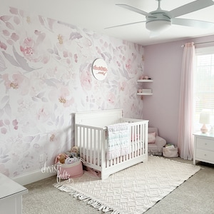 May include: A nursery with a white crib, a floral wallpaper, and a white ceiling fan. A pink rug and a pink basket with stuffed animals are in the room. The wall has a sign that says "Charlotte Avery".