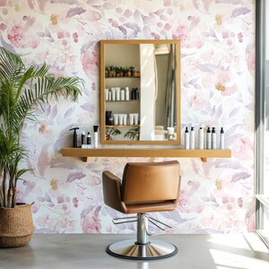 May include: A salon interior featuring a brown leather chair with a chrome base, a wooden-framed mirror, and a wooden shelf with beauty products. The background is a floral wallpaper in shades of pink and purple. A potted plant is in the corner.