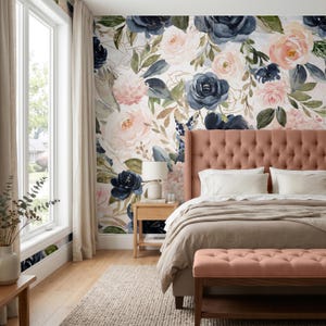 May include: A bedroom featuring a floral wallpaper mural with navy blue and blush pink roses, green leaves, and gold accents. A tufted salmon-colored headboard and matching bench sit in front of the wall, paired with white bedding and a beige throw.