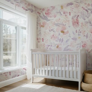 May include: A white crib in a nursery with floral wallpaper in shades of pink and purple. A window with white curtains is on the left. A woven basket is on the right. The room has a soft, inviting atmosphere.