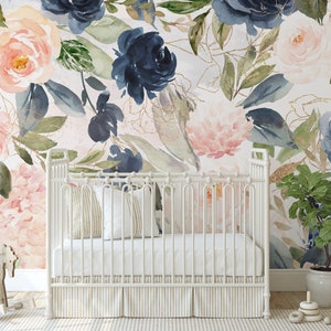 May include: A white crib with a striped skirt sits in front of a wall mural featuring large watercolor flowers in shades of navy blue, blush pink, and green with gold line accents. A wooden rocking horse and a potted plant are nearby.
