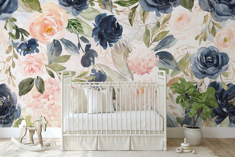 May include: A white crib with a striped skirt sits in front of a wall mural featuring large watercolor flowers in shades of navy blue, blush pink, and green with gold line accents. A wooden rocking horse and a potted plant are nearby.