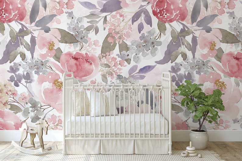 May include: A white crib with a striped skirt and pillows sits in front of a floral watercolor wallpaper. The wallpaper features large pink and purple flowers with gray and green leaves. A wooden rocking horse and a potted plant are in the foreground.