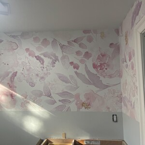 May include: Floral wallpaper featuring a watercolor design of pink and purple flowers and leaves on a white background. The wallpaper covers the wall and extends onto the adjacent wall. The lower portion of the wall is painted a light gray.