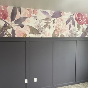 May include: A room with a floral wallpaper design in shades of pink, purple, and white. The lower portion of the wall features dark gray paneling with a simple, modern design. Electrical outlets are visible.