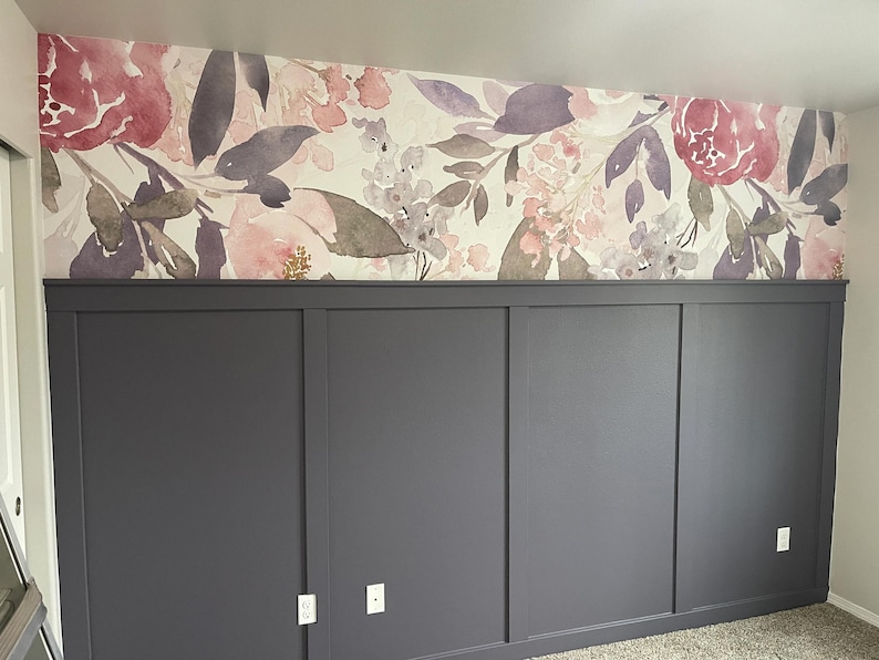 May include: A room with a floral wallpaper design in shades of pink, purple, and white. The lower portion of the wall features dark gray paneling with a simple, modern design. Electrical outlets are visible.