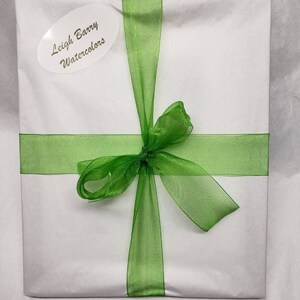 May include: A square package wrapped in white paper and tied with a bright green sheer ribbon. An oval sticker on the front reads "Leigh Barry Watercolors". The ribbon is tied in a bow.