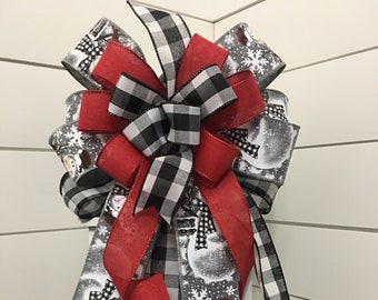 May include: A red, black and white plaid bow with a snowman print ribbon. The bow is tied on a white lantern.