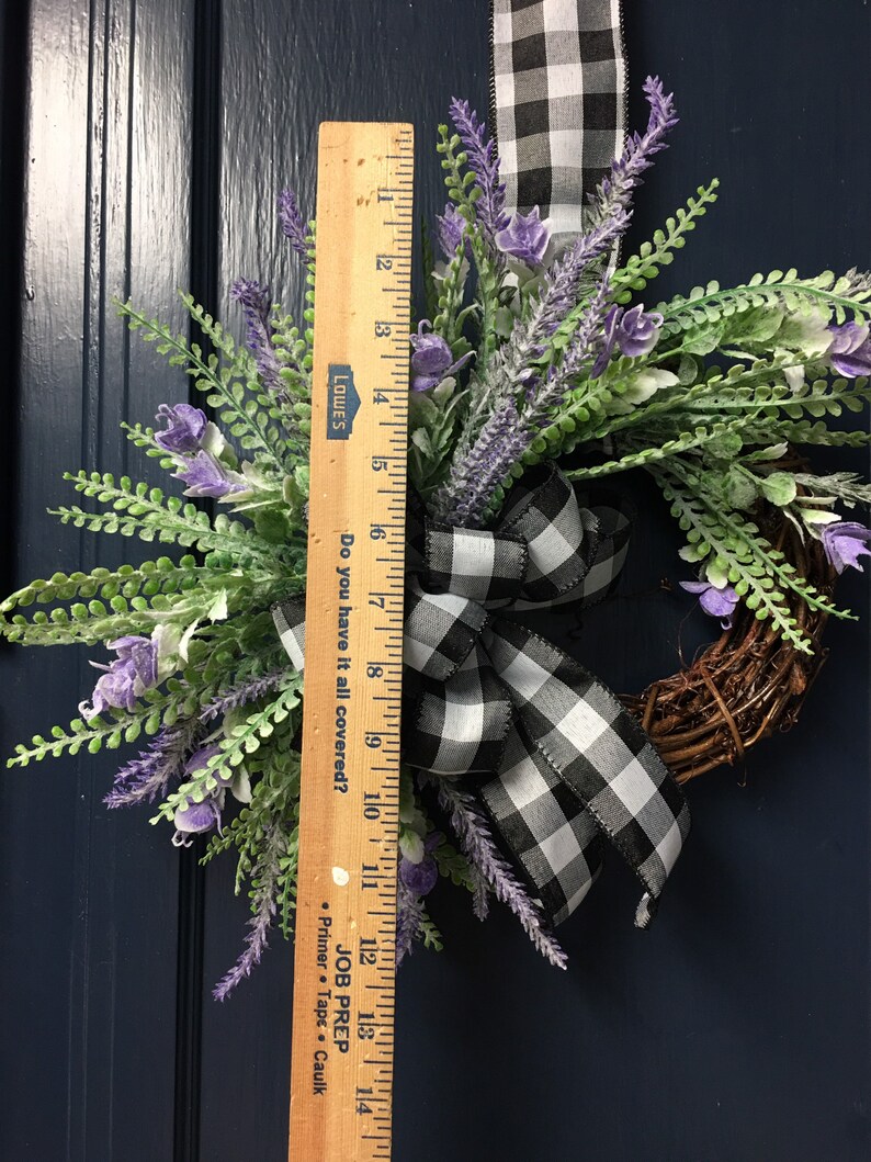 May include: A black and white checkered ribbon tied around a wreath of lavender sprigs. The wreath is 14 inches in diameter. The wreath is hanging on a dark blue door.